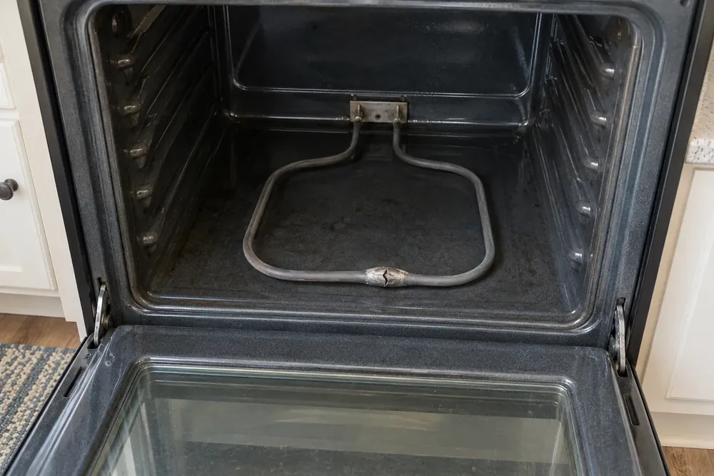 Electric oven bake element with a split, blistered spot near its middle, door lowered open