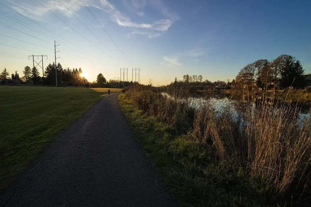Paved path beside Bethany Lake at sunset with power lines and autumn trees, Oregon