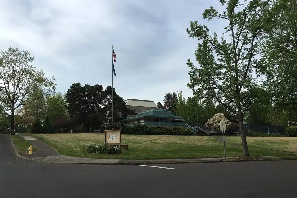 Lawn, flagpole and recreation center among tall trees at a street corner in Oak Hills, Oregon