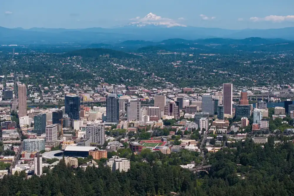 Drone view of downtown Portland, Oregon, its towers and wooded hills, with Mount Hood beyond