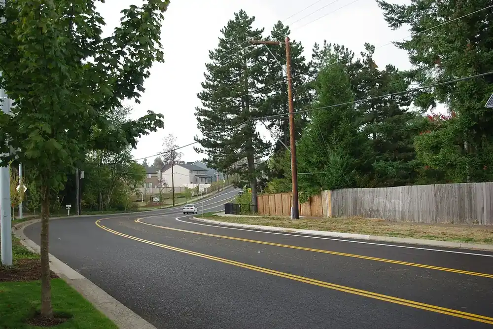 Curving Bull Mountain Road lined with young trees and a wooden fence in Tigard, Oregon
